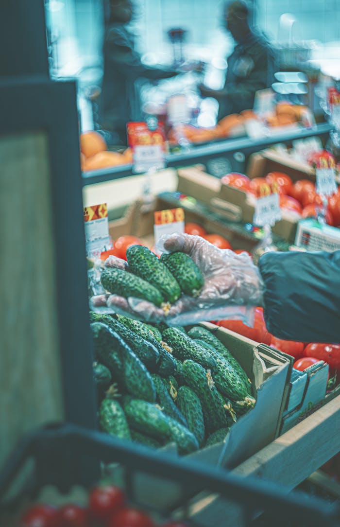 Man choosing fresh cucumbers at a bustling farmer's market indoors.
