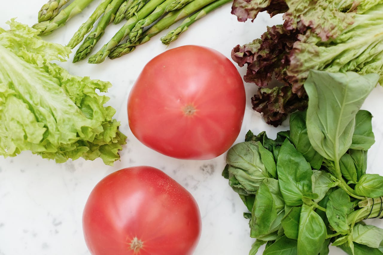 Top view of fresh vegetables including tomatoes, asparagus, lettuce, and basil on a marble surface.
